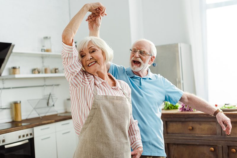 An elderly couple dancing in their kitchen while they cook dinner